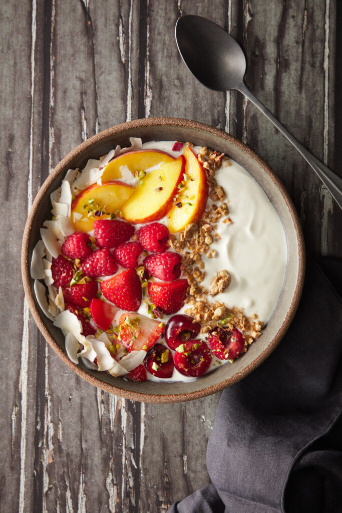 bowl de yogur, frutas y granola sobre fondo de madera gris